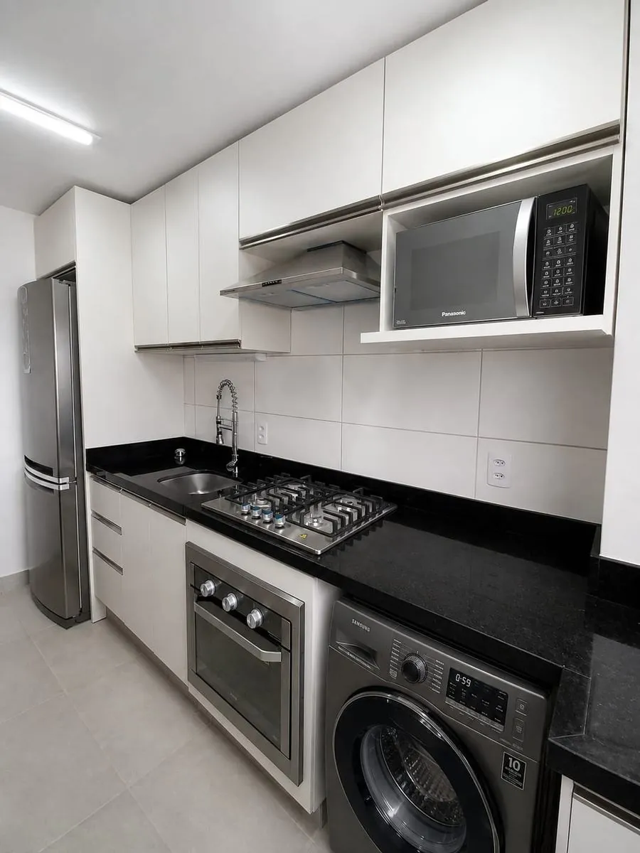 Cozinha planejada branca com bancada preta e lavanderia integrada